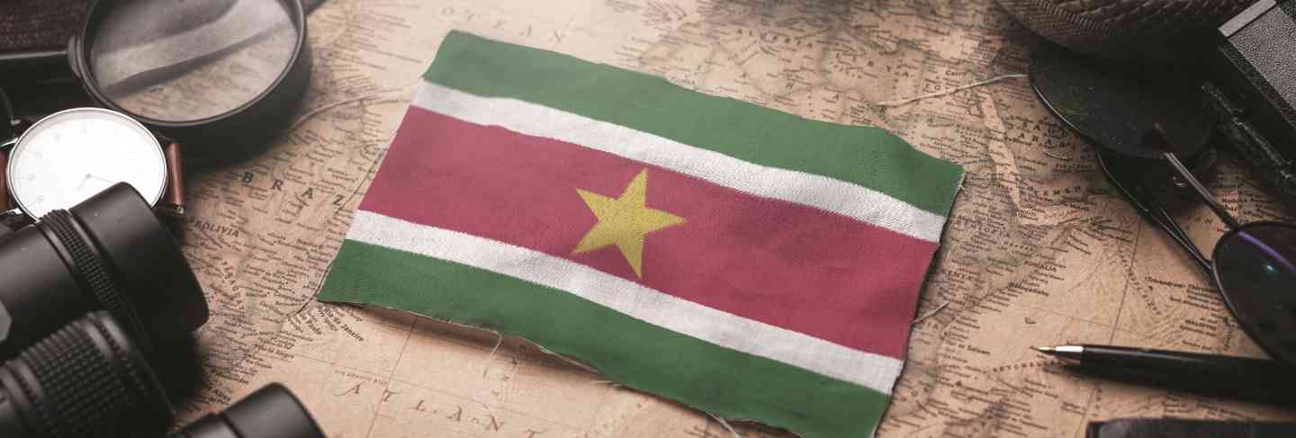 Suriname flag between traveler's accessories on old vintage map. tourist destination concept.
